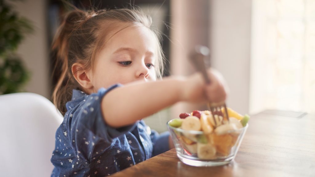 A young girl eats bananas and berries in a glass bowl with a fork. Searching for a functional child nutritionist near me can have life-changing results with Eat for Life.