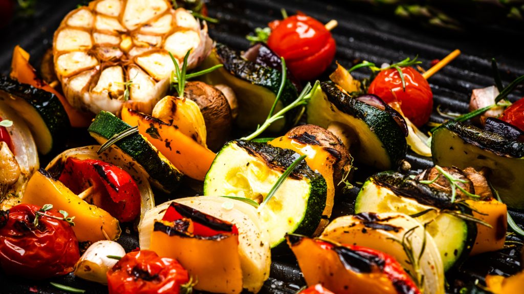 An up-close image of vegetables being grilled on a charcoal grill.