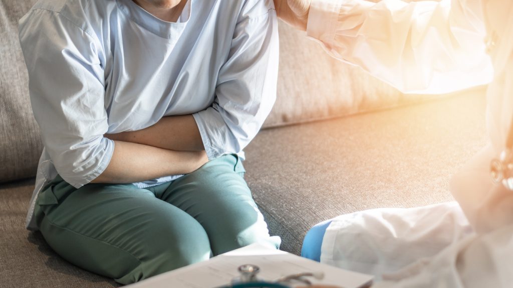 A woman sits on a couch and holds her stomach. Gut health diet near me.