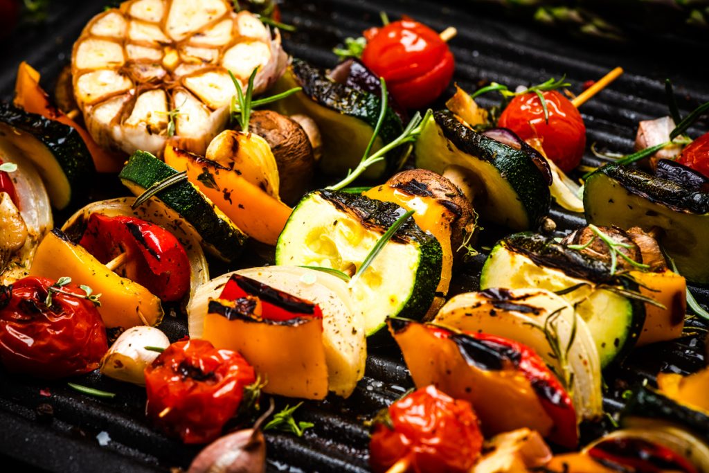 An up-close image of vegetables being grilled on a charcoal grill.