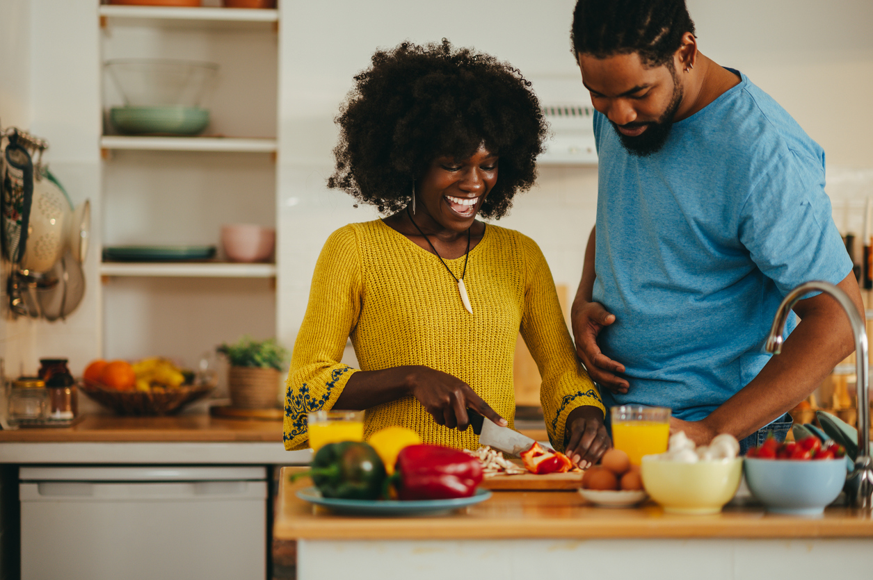 A couple cooks a meal together, they are both smiling and happy.