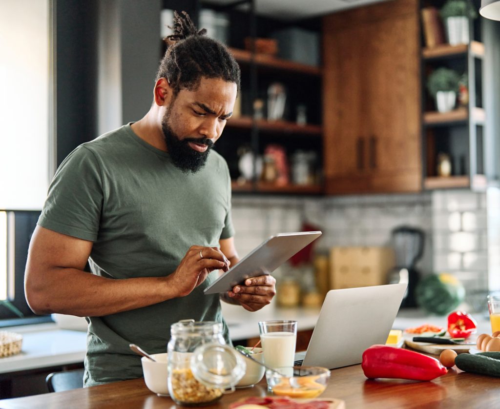 A man is cooking in his kitchen while checking his tablet for a recipe.