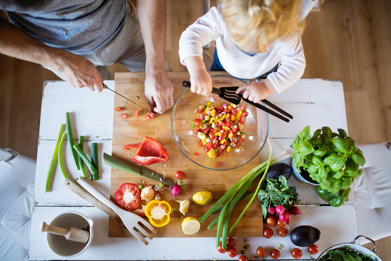 a man and a small child are cutting up vegetables and making salsa at a table. As a child nutritionist, I recognize how much you care about your child's health.