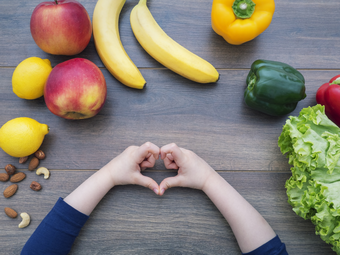 id making heart shape on a table full of healthy food. As a child nutritionist, I am eager to help your family achieve your goals.