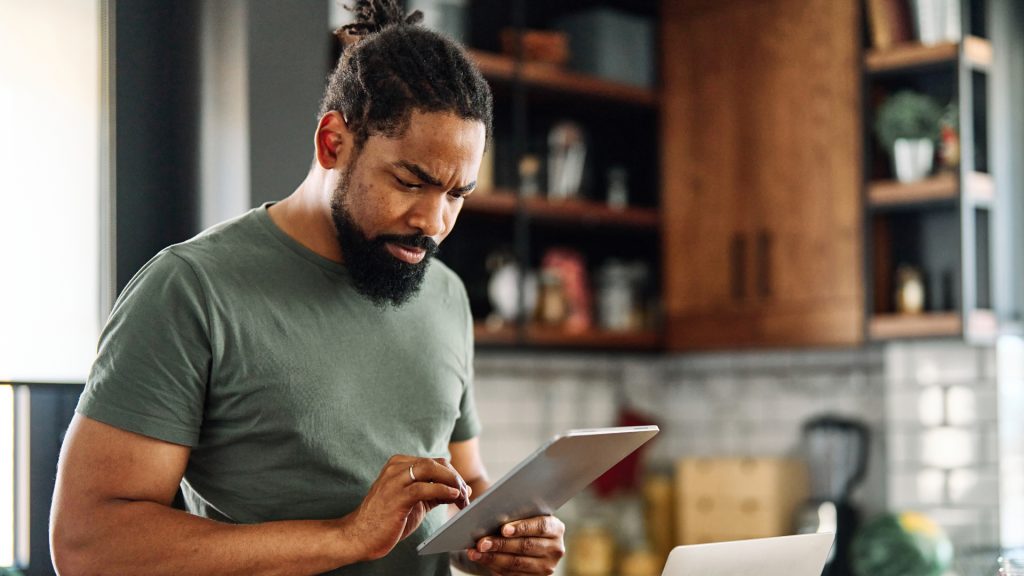 A man is cooking in his kitchen while checking his tablet for a recipe.