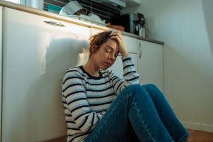 A young woman sits with her head in her band, she appears stressed. In this article we discuss how to regulate cortisol levels, the difference between high and low cortisol levels, and how to check cortisol levels.