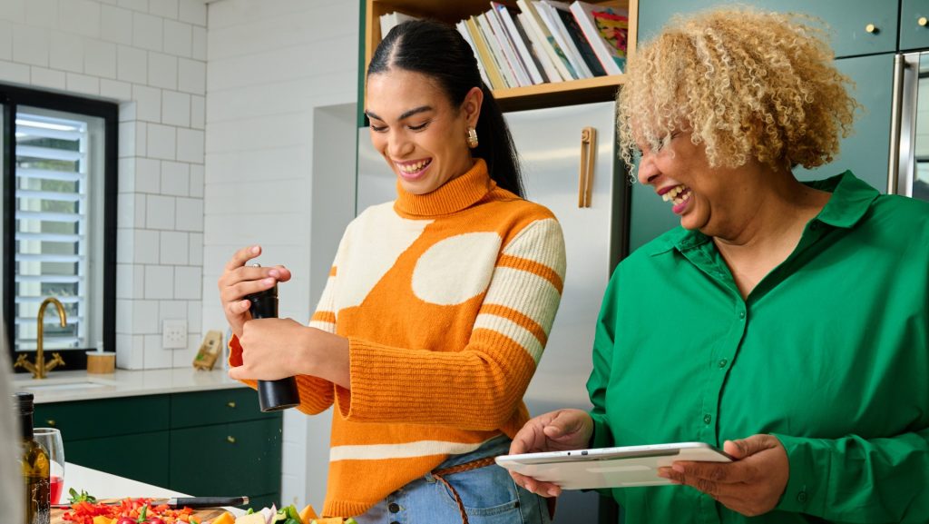 Two smiling women cook together in a kitchen.